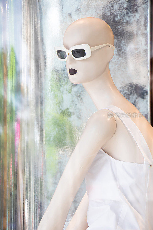 一个穿着白色裙子的人体模型娃娃在Max Mara商店的橱窗里倒影